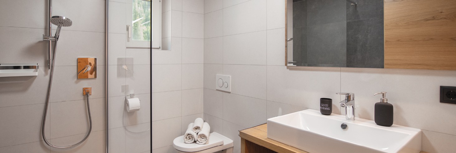 Bagno con moderna cabina doccia in vetro, piastrelle chiare e morbidi asciugamani