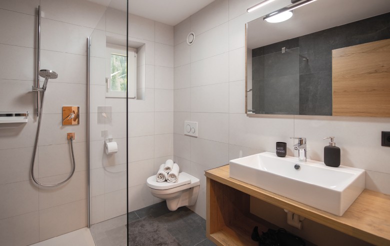 Bagno con moderna cabina doccia in vetro, piastrelle chiare e morbidi asciugamani